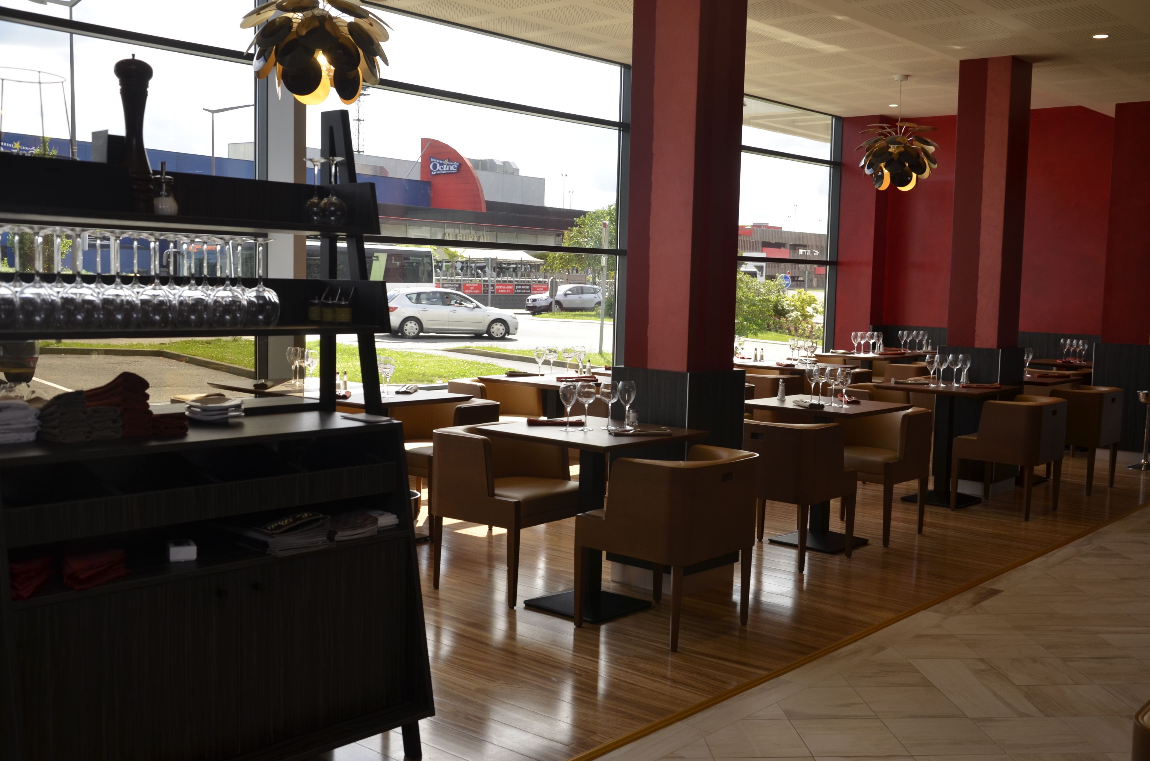 Een restaurantinterieur met tafels en stoelen, een bar met glazen en flessen, en een uitzicht op het buitengebeuren door grote ramen.
