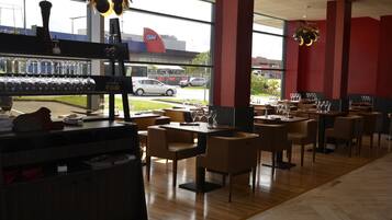 Een restaurantinterieur met tafels en stoelen, een bar met glazen en flessen, en een uitzicht op het buitengebeuren door grote ramen.