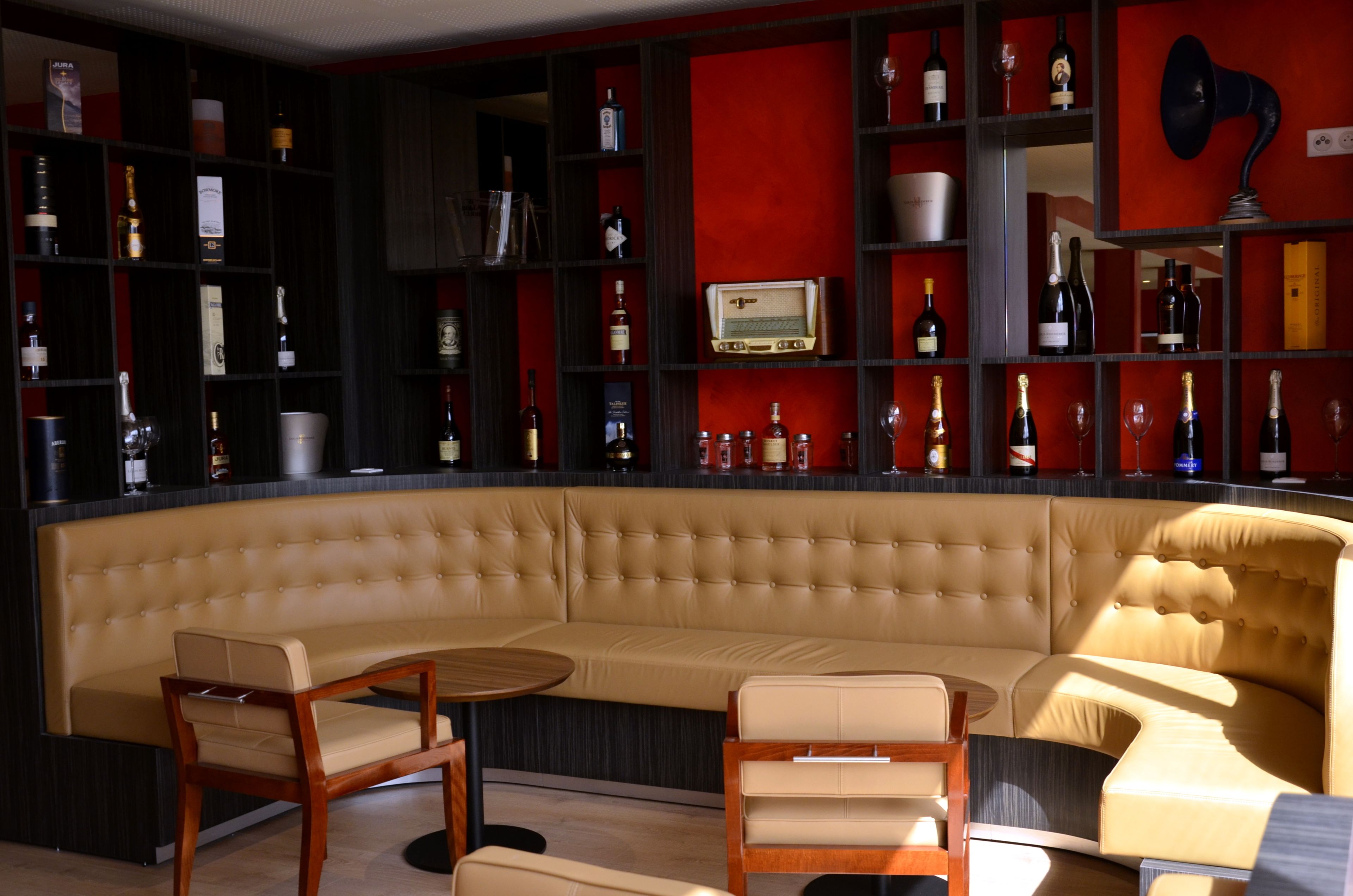A modern lounge area with a curved sofa, wooden chairs, and a red accent wall.