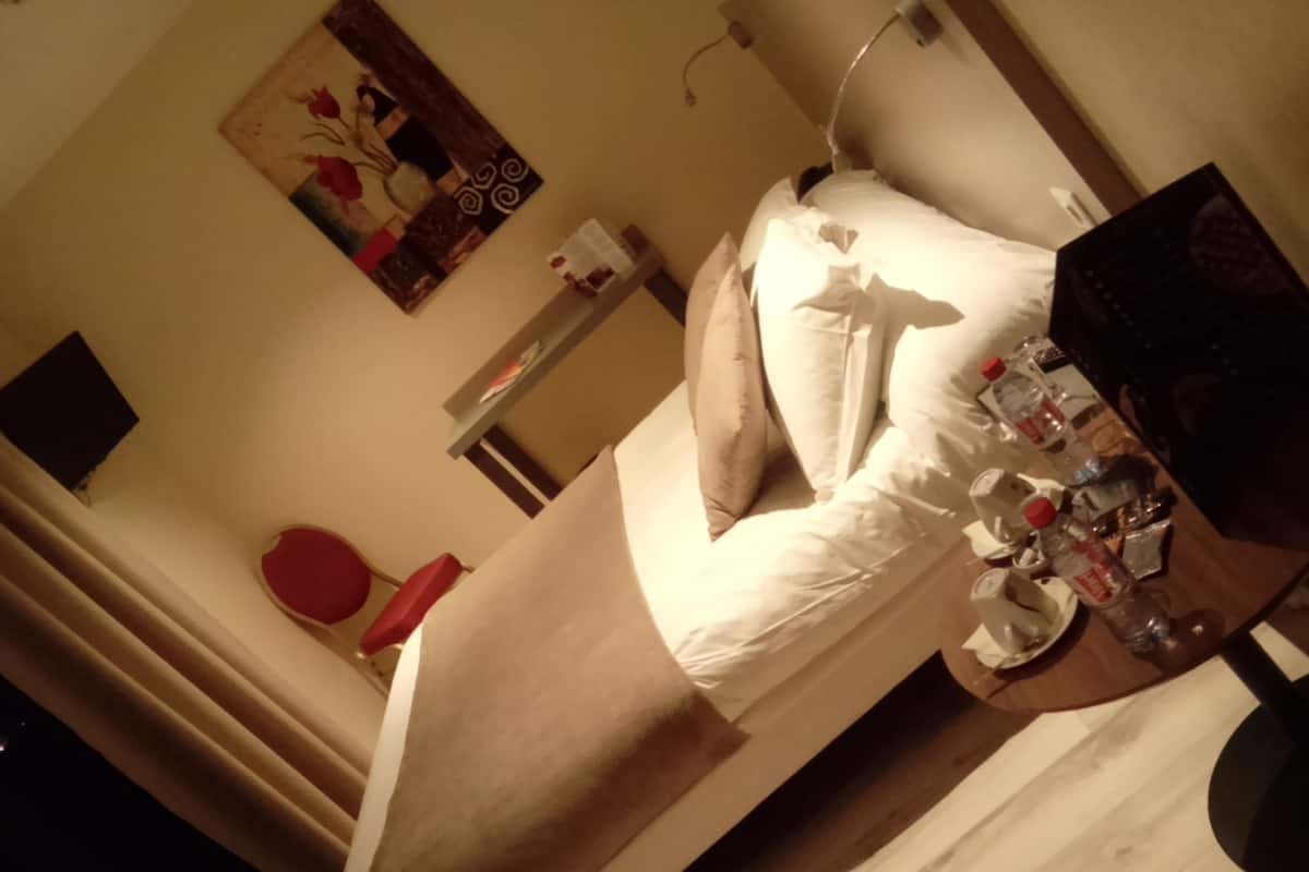 A hotel room with a bed, bedside table, and a painting on the wall.