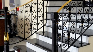 Uma escadaria com guarda-corpos em preto e dourado, degraus de mármore e corrimão.