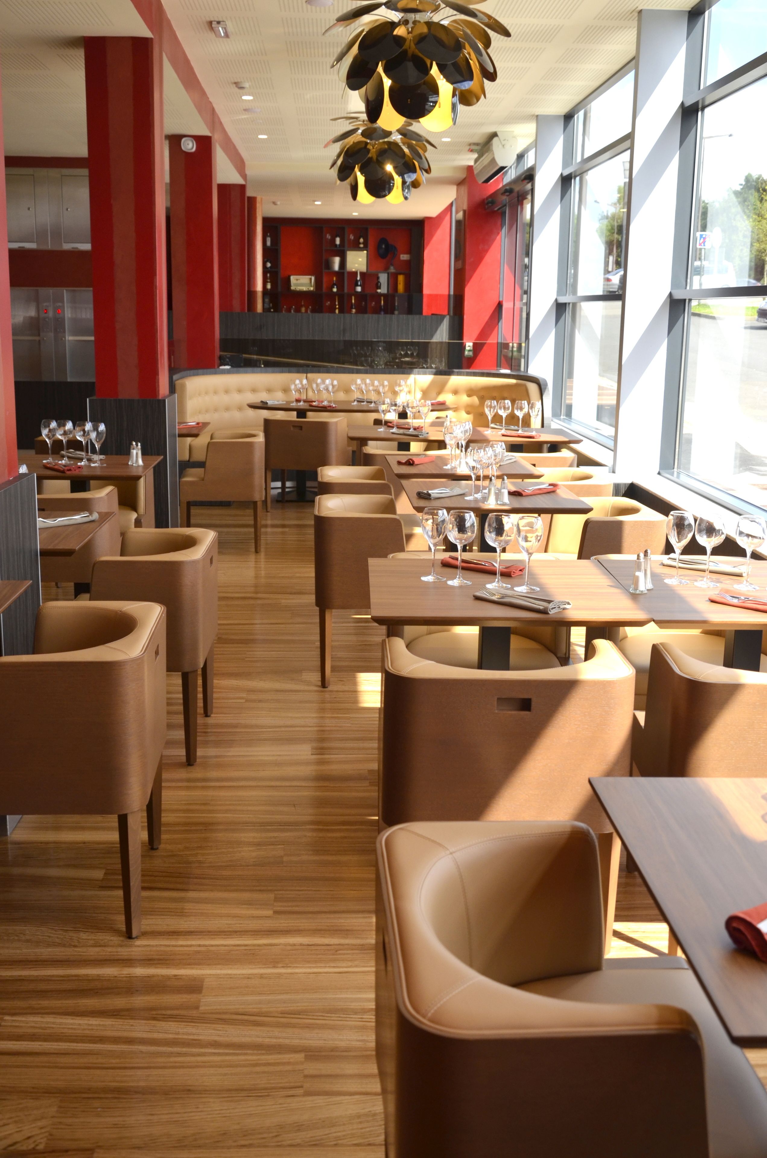 A modern restaurant with wooden floors and beige chairs. Tables are set with wine glasses and cutlery.