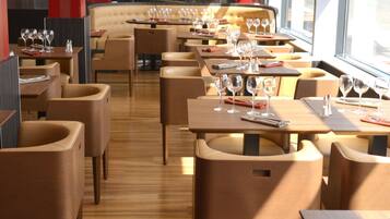 Un restaurante moderno con suelos de madera y sillas color beige. Las mesas están dispuestas con copas de vino y cubiertos.