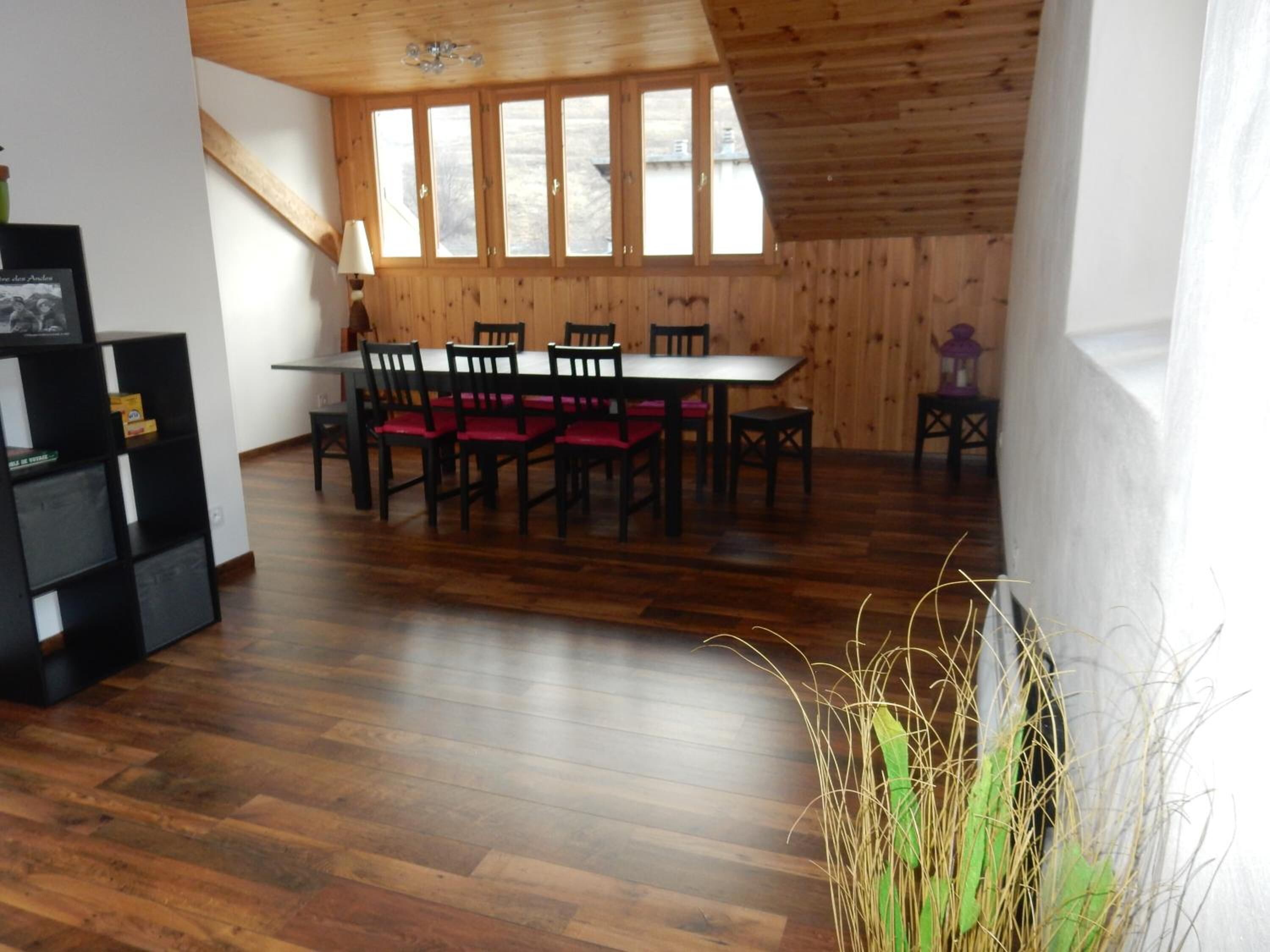 Un comedor con una mesa y sillas de madera, una estantería y vistas amplias a través de grandes ventanales.
