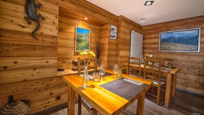 A wooden-paneled room with a dining table set for four, a framed painting on the wall, and a wooden sculpture. - Hôtel Châlet de Lanza (Abriès-Ristolas)