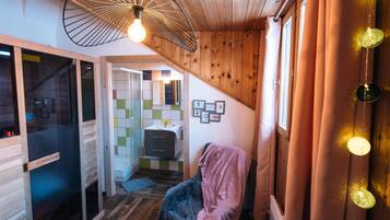 A cozy room with a wooden ceiling, a hanging light fixture, a bed, and a small table.
