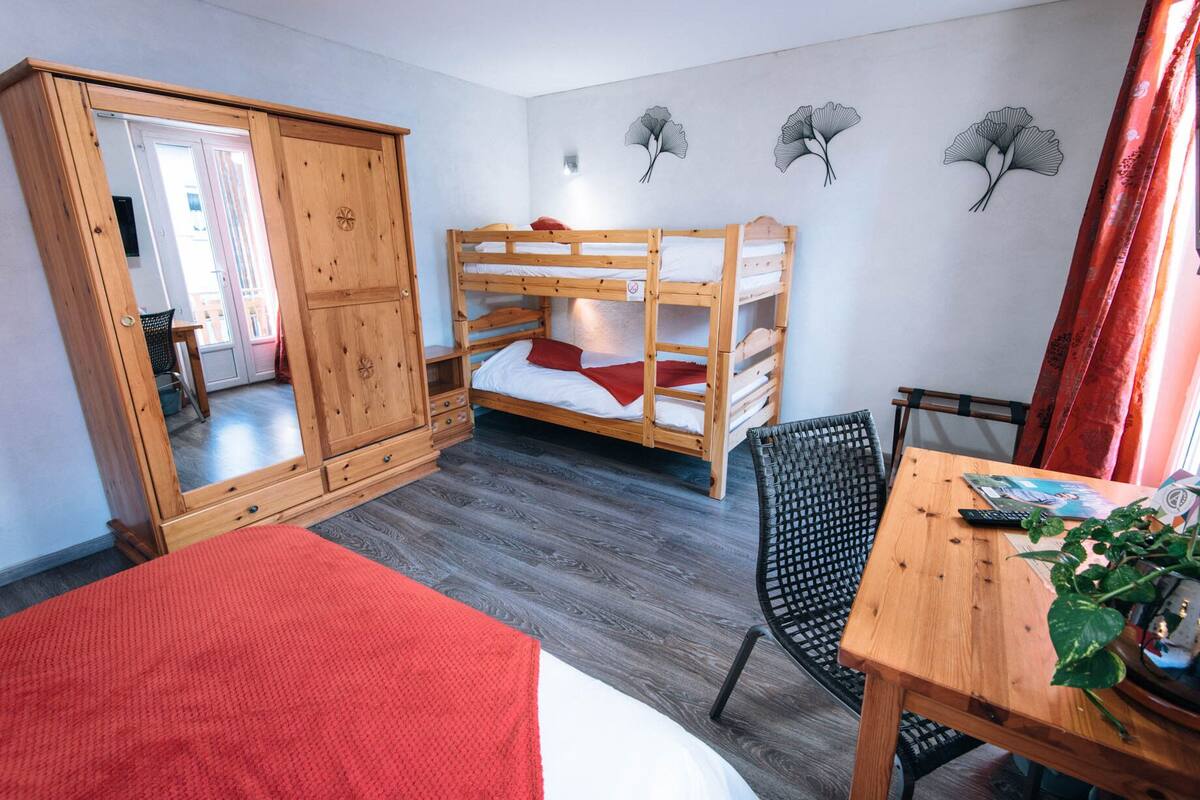 A room with a bunk bed, a wooden wardrobe, a dining table, and a chair.