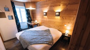 A cozy bedroom with a wooden headboard, a large bed with a knitted blanket, bedside lamps, and a wooden floor. - Hôtel Châlet de Lanza (Abriès-Ristolas)
