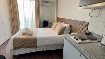 Una habitación de hotel con cama, escritorio, silla, kitchenette y aire acondicionado.