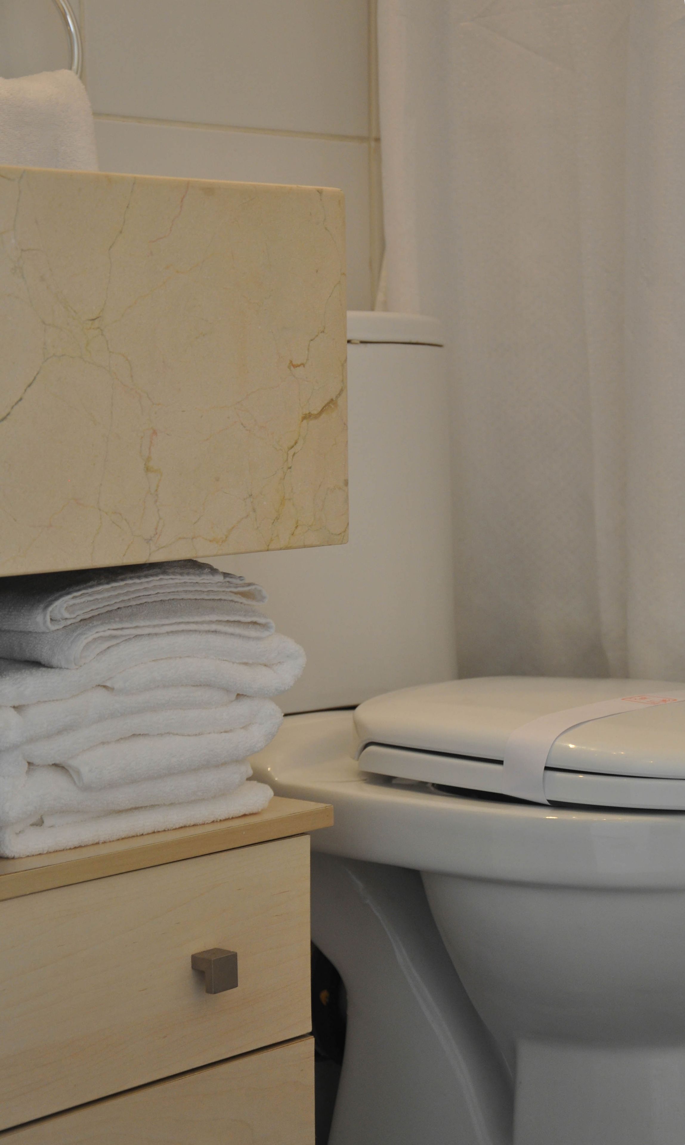 A bathroom with a marble vanity, a stack of white towels, and a toilet.