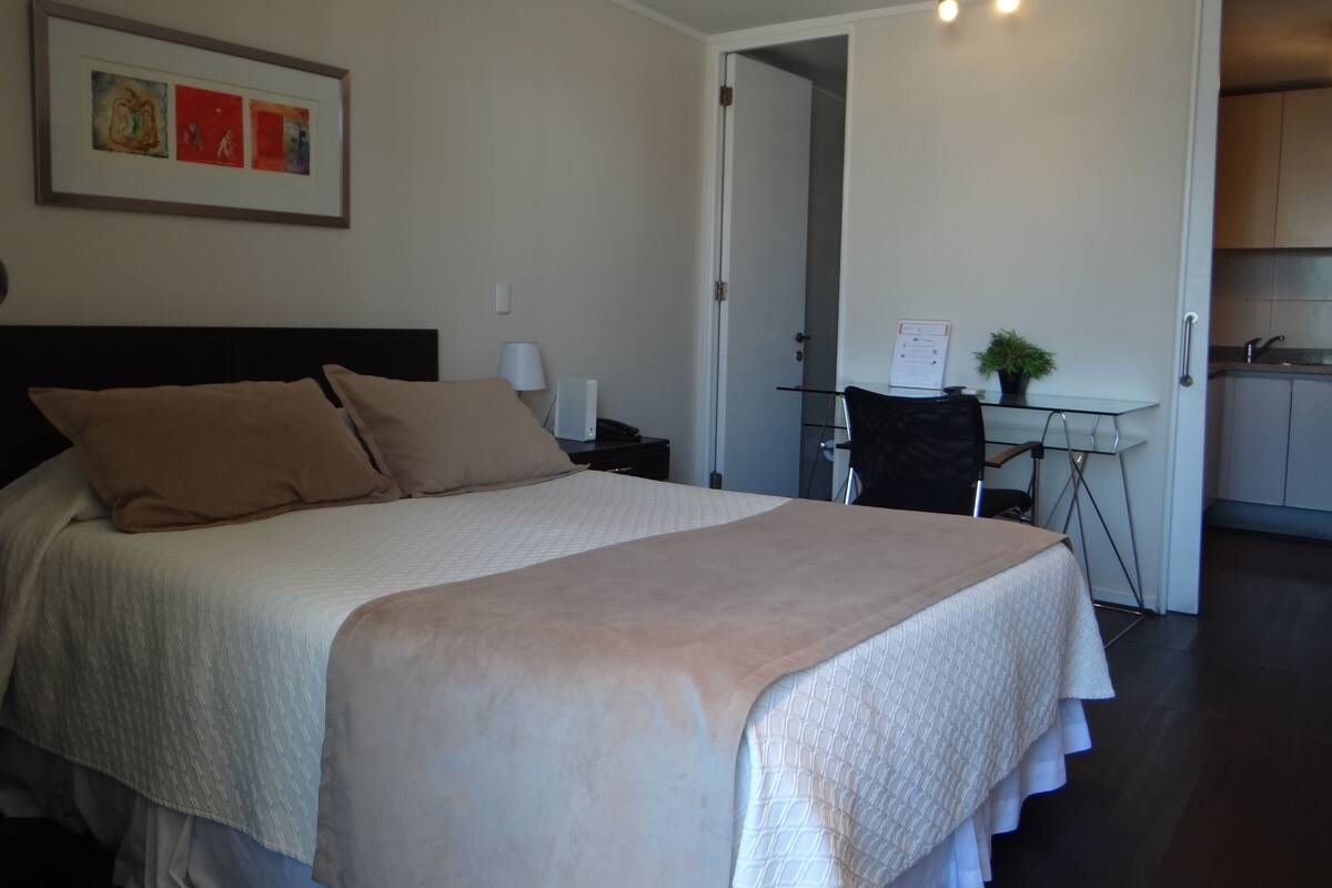 A hotel room with a bed, a desk, and a kitchenette.