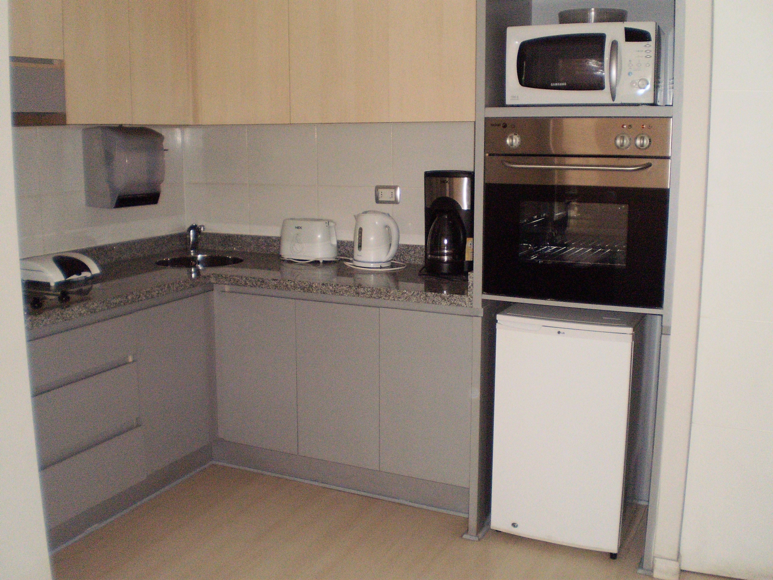 Una cocina compacta con microondas, cafetera, tostadora y un refrigerador pequeño.