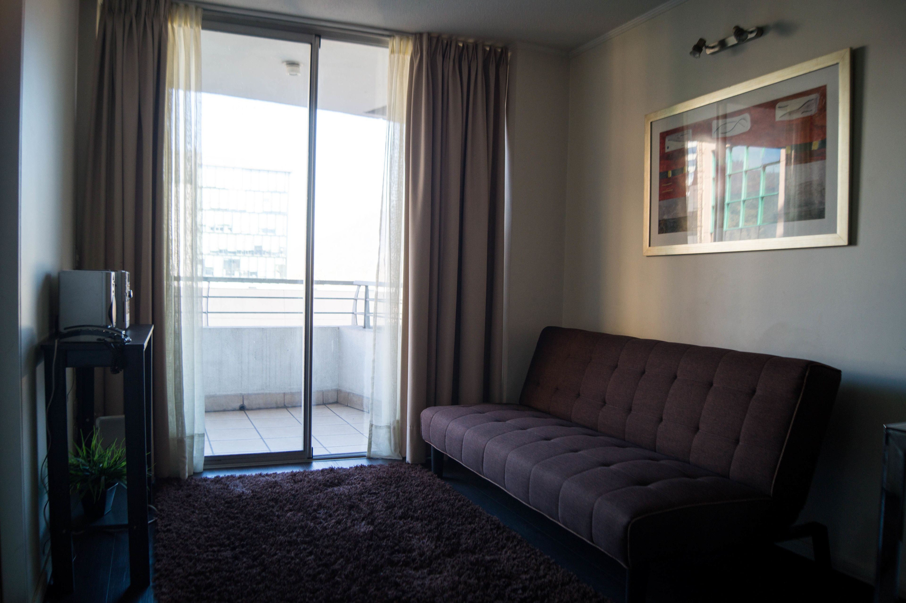 A living room with a sofa, a TV stand, and a sliding glass door leading to a balcony.