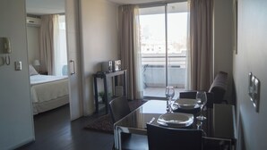 A hotel room with a bed, a dining area with a table set for two, a small table with a radio, and a view of the outside balcony. - Rentasuite (Santiago)