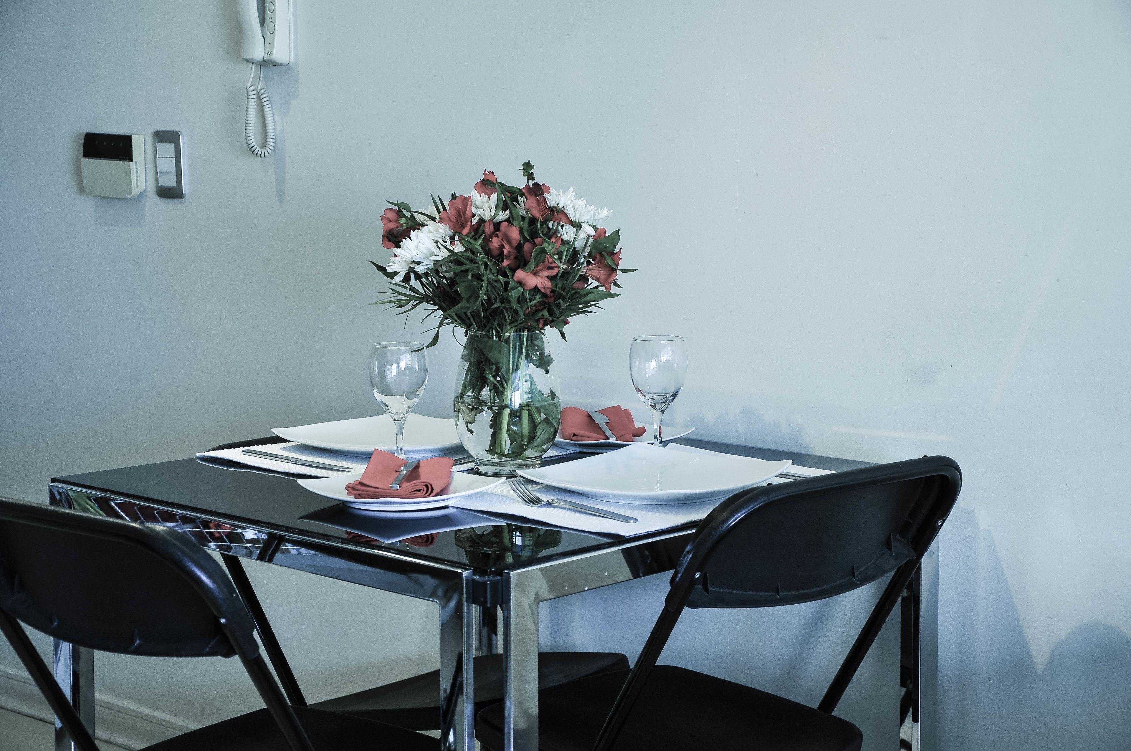 A dining table set with white plates, red napkins, and a vase of flowers.
