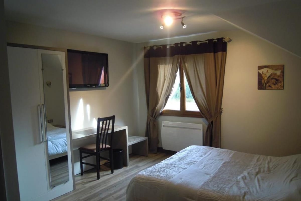 Un dormitorio con cama, escritorio, silla, televisor y ventana con cortinas.