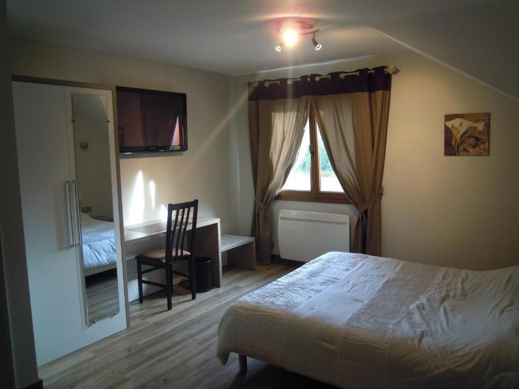 Une chambre à coucher comprenant un lit, un bureau, une chaise, un téléviseur et une fenêtre avec des rideaux.