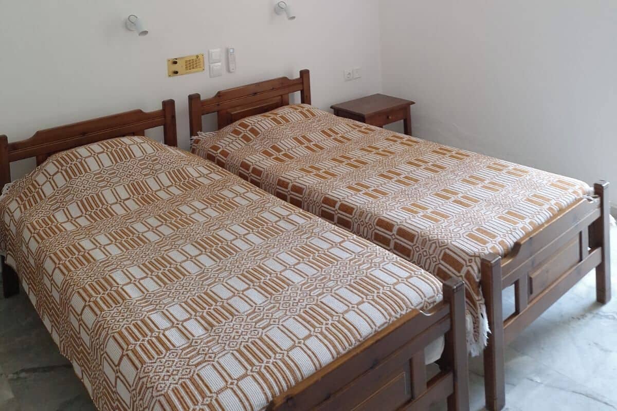 Una habitación con dos camas de madera, un ventilador de techo y una pared blanca.