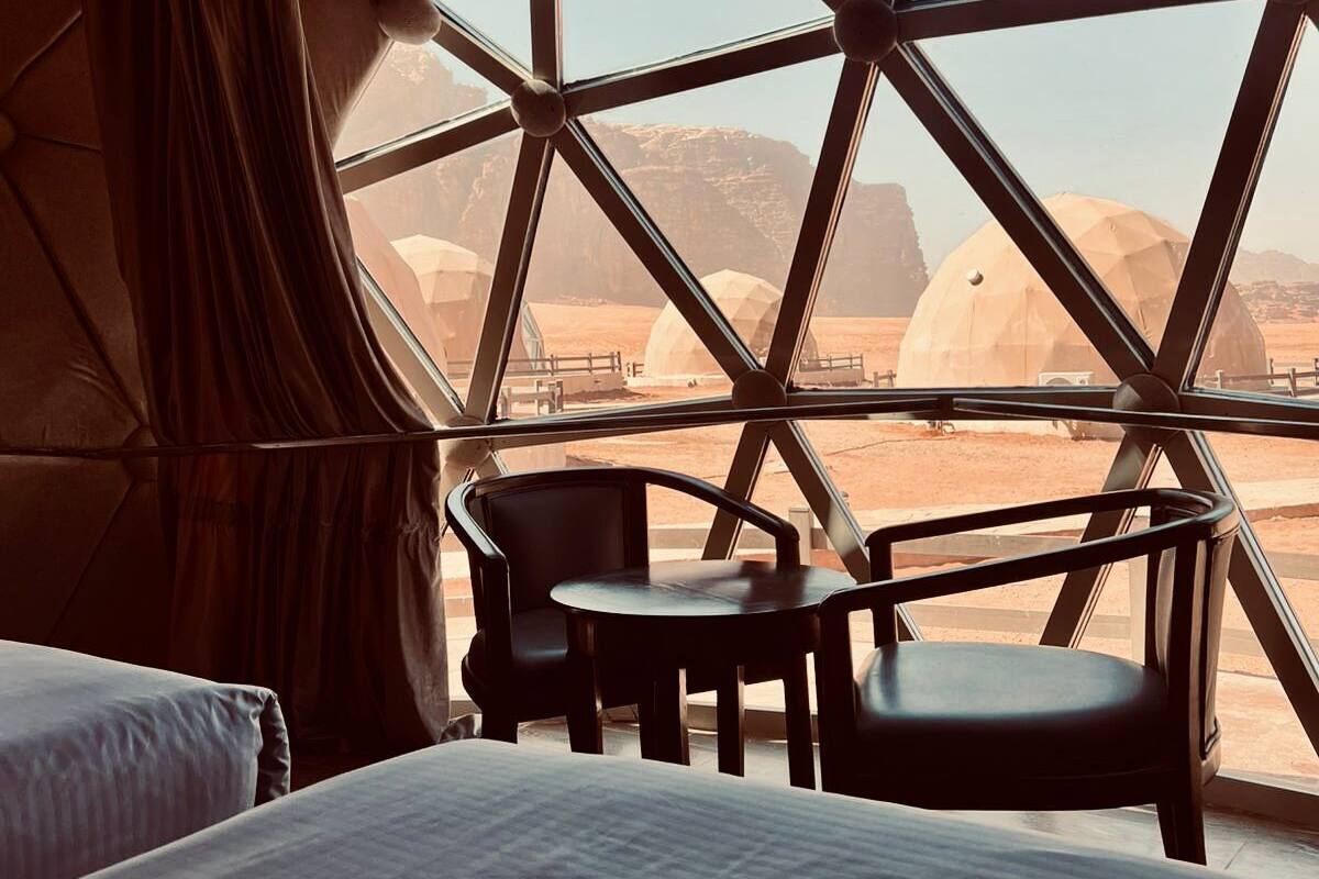 A room with a bed, two chairs, and a large window with a view of a desert landscape.