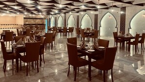 A spacious restaurant with high ceilings and modern chandeliers, featuring a central dining area with tables and chairs, and a patterned wall in the background. - Beyond Wadi Rum Camp (Wadi Rum)