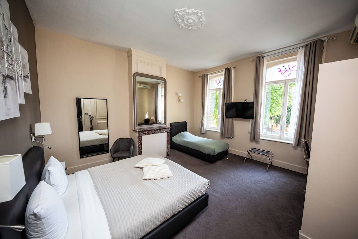A hotel room with a bed, a desk, a chair, a TV, and a window with curtains.