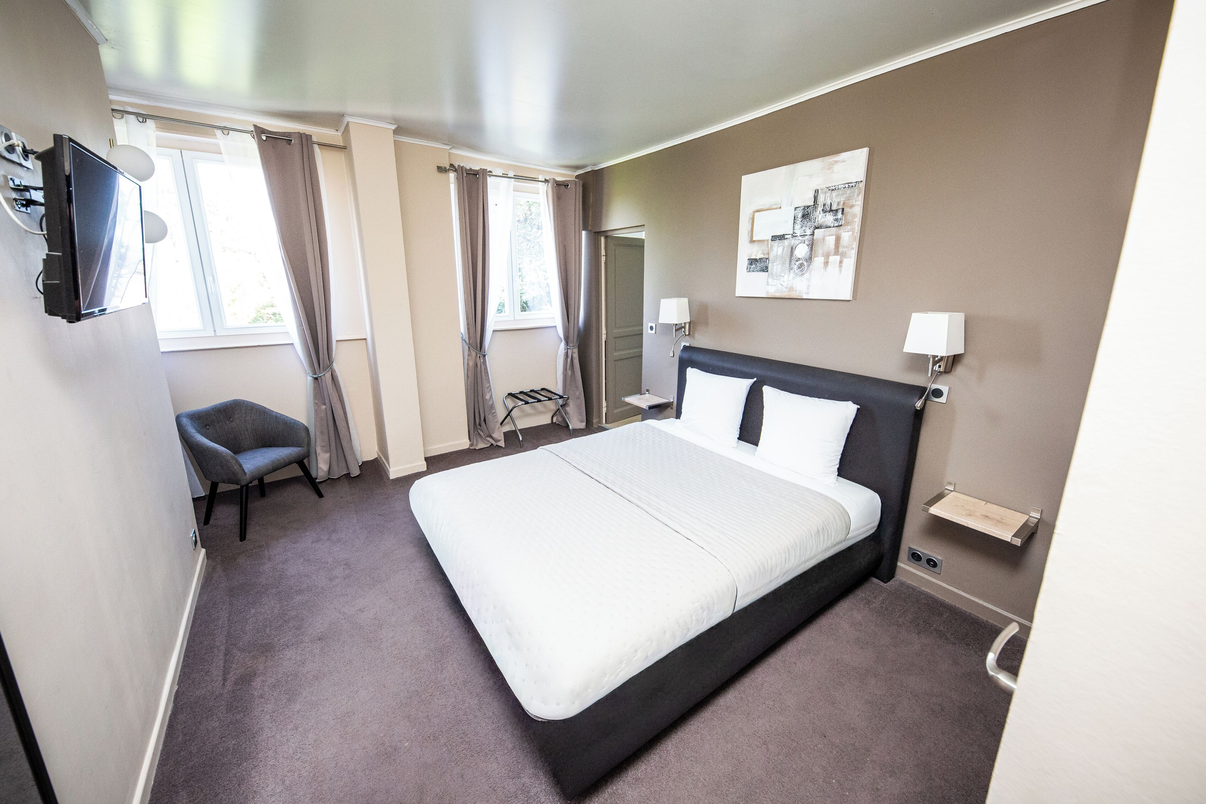 Een hotelkamer met een groot bed, een stoel, een televisie en een raam met gordijnen.