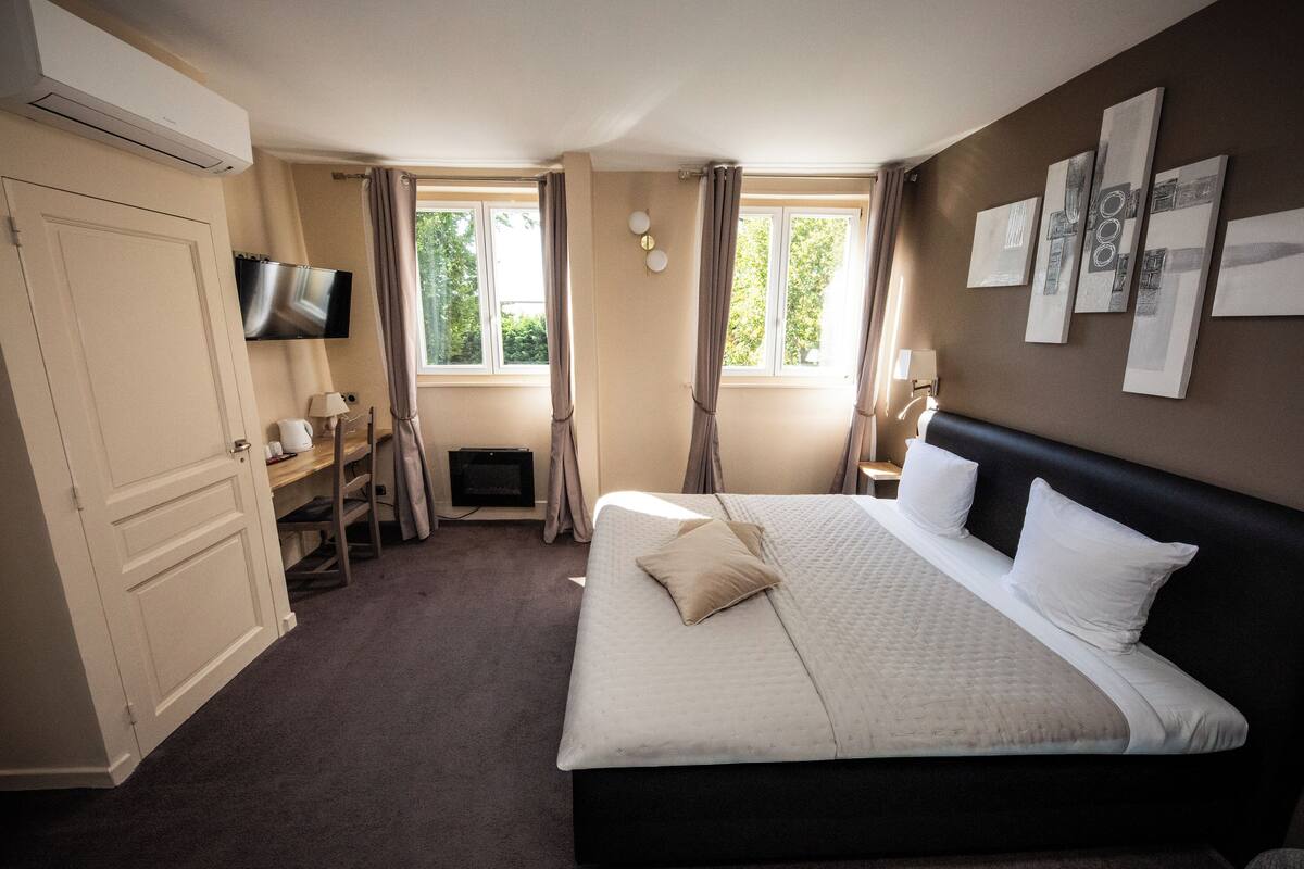 A hotel room with a large bed, a desk, a chair, a TV, and a window with curtains.