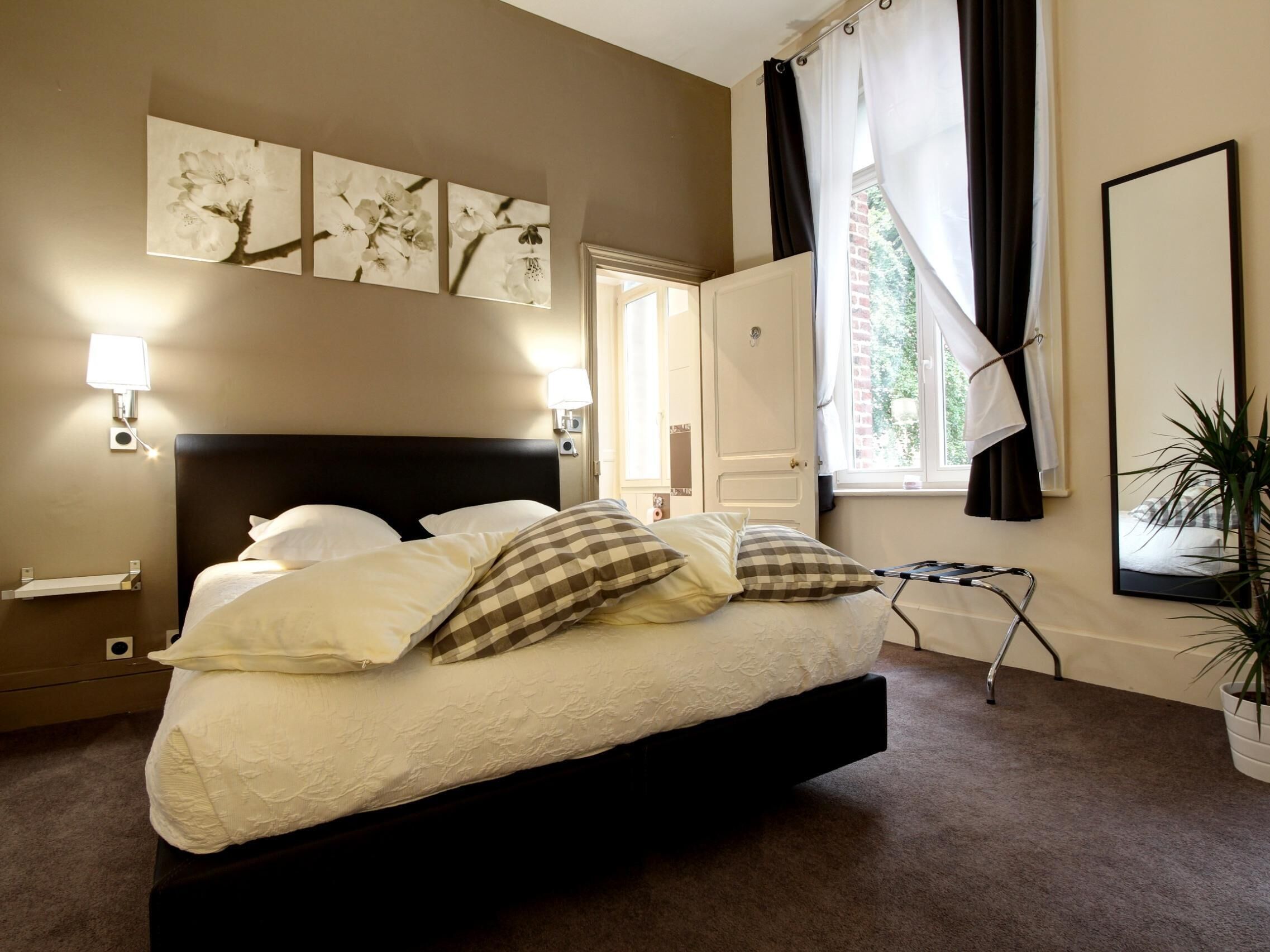 Une chambre à coucher avec un grand lit, deux lampes fixées au mur, un miroir et des œuvres d’art au-dessus du lit.
