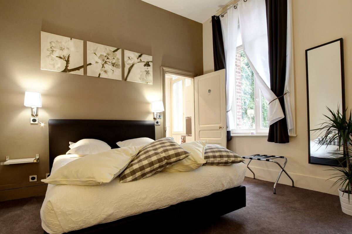 A bedroom with a large bed, two wall-mounted lamps, a mirror, and a window with curtains.