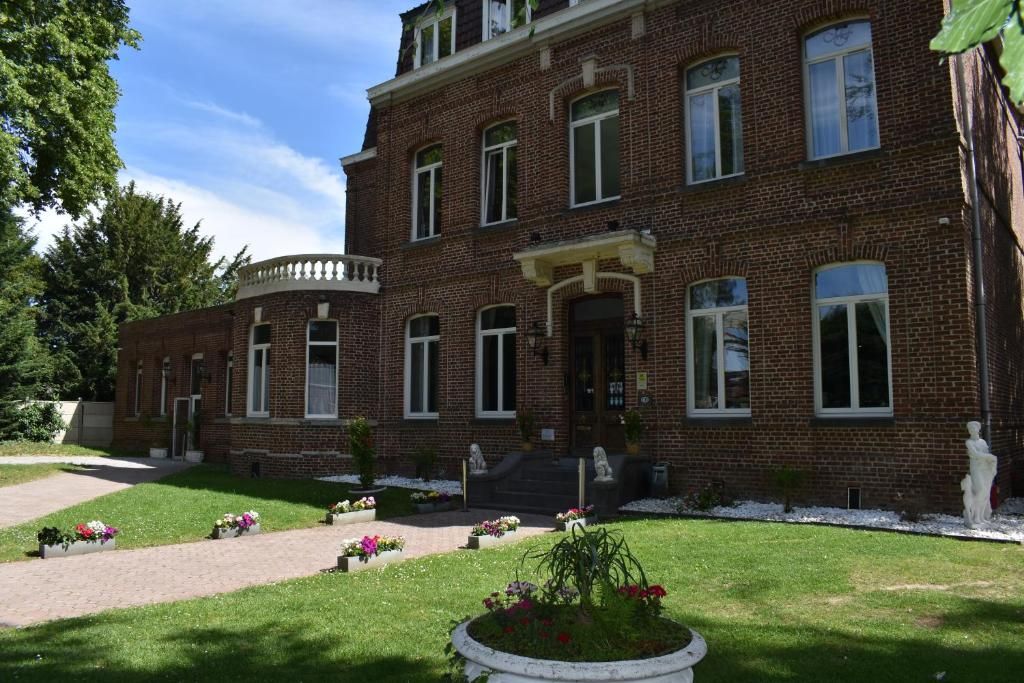 A two-story brick building with a symmetrical facade, a central entrance with steps, and a small garden area with flower beds.