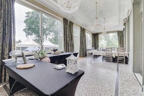 Un comedor amplio con una mesa larga dispuesta para varios comensales, ventanas grandes con cortinas y un candelabro.