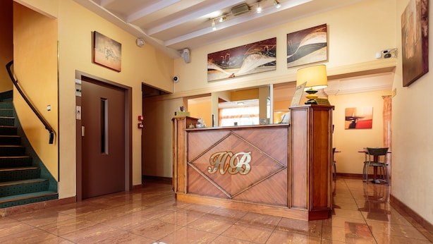 A reception area with a wooden reception desk, a staircase, and a tiled floor. - Hotel de Bordeaux (Clermont-Ferrand)