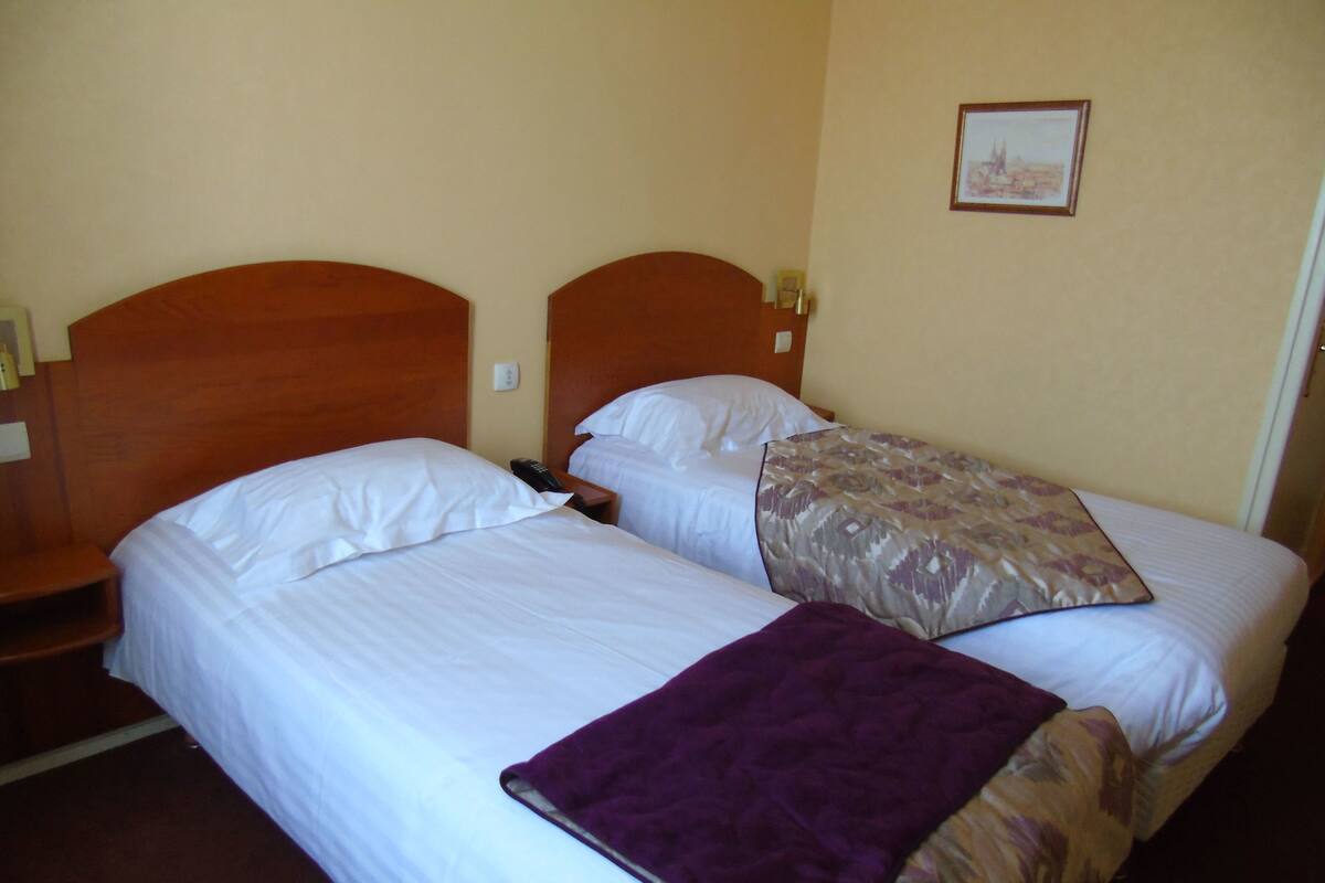 A hotel room with two beds, a wooden headboard, a nightstand, and a framed picture on the wall.