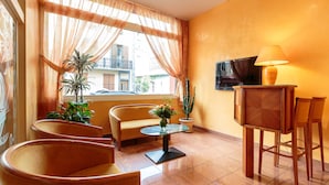 A hotel room with a sofa, chairs, a small table, a TV, and potted plants. - Hotel de Bordeaux (Clermont-Ferrand)