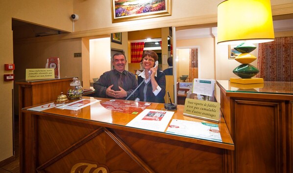 A hotel reception desk with a wooden finish, a glass partition, and a sign indicating the hotel is not famous. - Hotel de Bordeaux (Clermont-Ferrand)