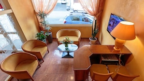 A hotel room with a seating area, a TV, and a desk with a lamp. - Hotel de Bordeaux (Clermont-Ferrand)