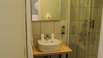 Un baño con lavamanos, espejo y ducha con mampara de vidrio.
