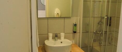Un baño con lavamanos, espejo y ducha con mampara de vidrio.