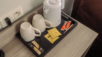 Une chambre d’hôtel avec une table en bois, un plateau sur lequel se trouvent une tasse blanche, une machine à café blanche et quelques sachets de thé.