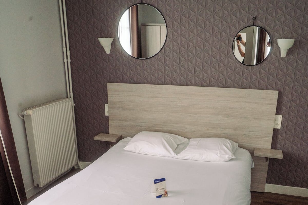 Ein ordentlich bezogenes Bett mit weißen Leinentüchern, einem hölzernen Kopfteil und zwei an der Wand befestigten Spiegeln.