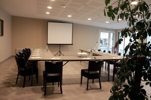 Un salón de conferencias con una mesa larga, sillas, una pantalla de proyector y una planta en primer plano.