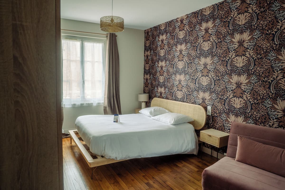 Ein Schlafzimmer mit einem Bett, einem Nachttisch, einer Lampe, einem Sessel und einer Wand mit Musterung.