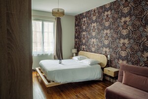 Un dormitorio con cama, mesita de noche, lámpara, silla y un papel tapiz estampado.