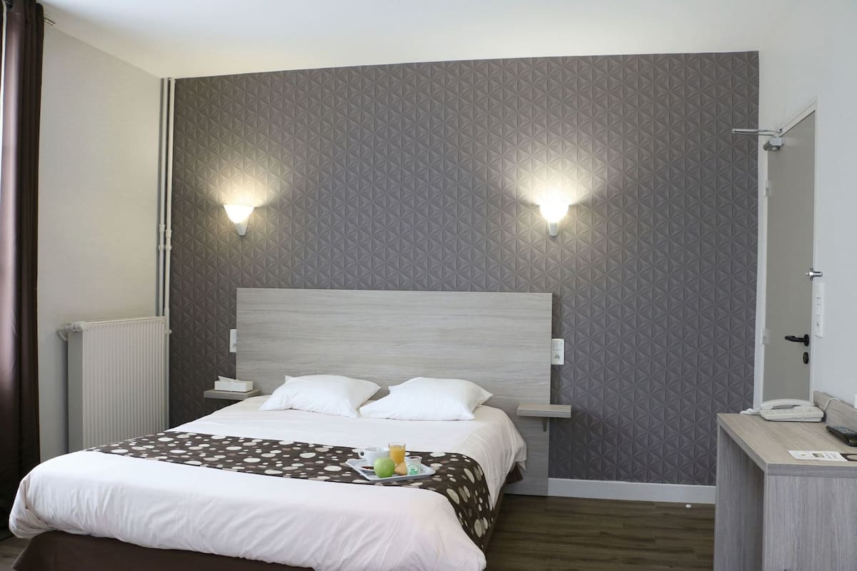 Ein Hotelzimmer mit Bett, Nachttischen, einer Wandlampe und einem Spiegel.