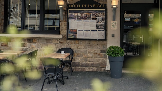 A hotel exterior with outdoor seating, a sign reading "HOTEL DE LA PLACE", and a lamp post. - Hotel De la Place (Les Monts d'Aunay)