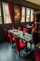 Un interior de restaurante con sillas de terciopelo rojo, un gran jarrón de metal y un piso de baldosas.