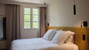 Un letto rifatto con lenzuola bianche, una finestra con tende e un lampadario a parete.