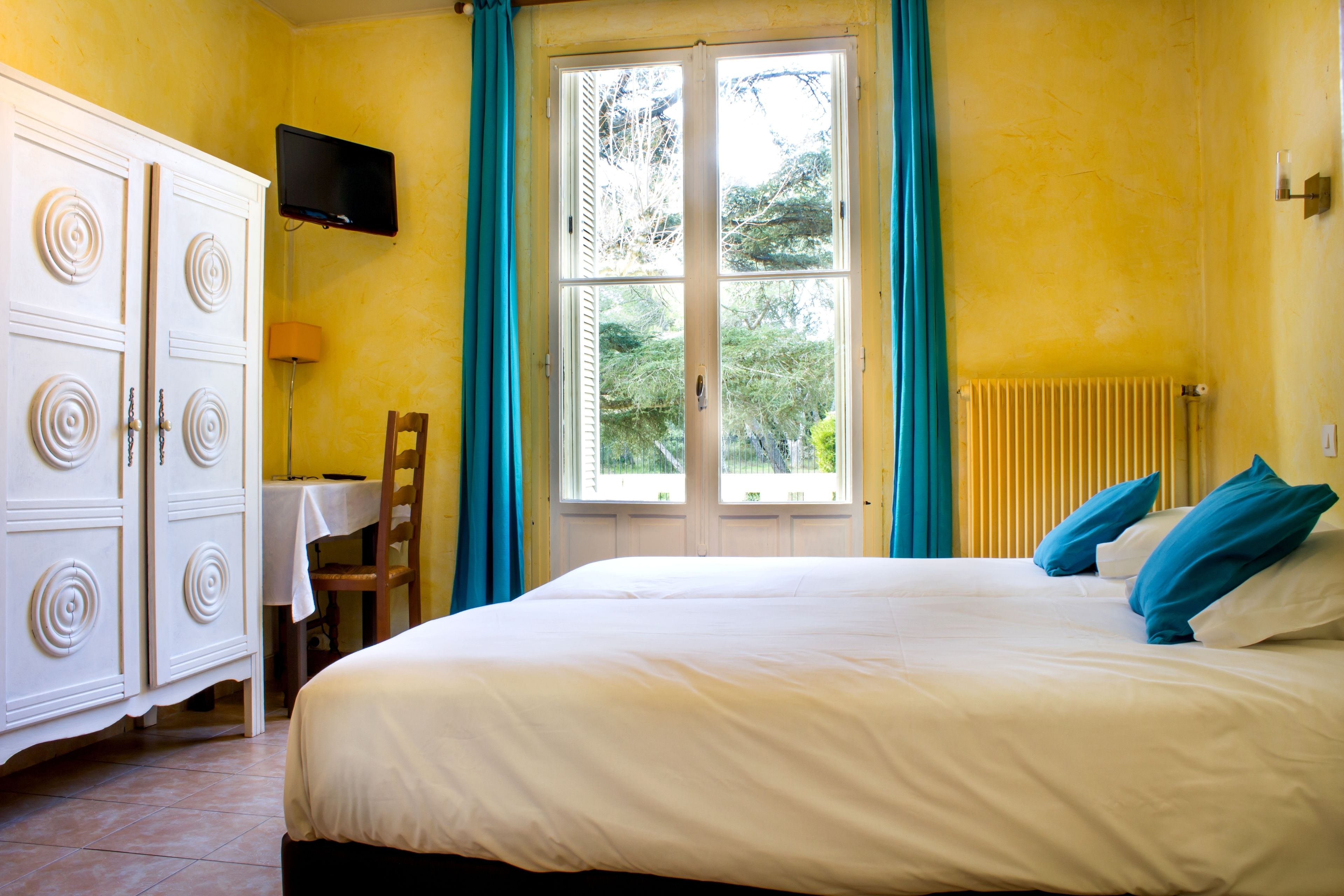 A bedroom with a bed, a desk, a chair, a wardrobe, and a window with curtains.