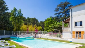 Una piscina con lettini, un'area salotto coperta e un edificio con un balcone.