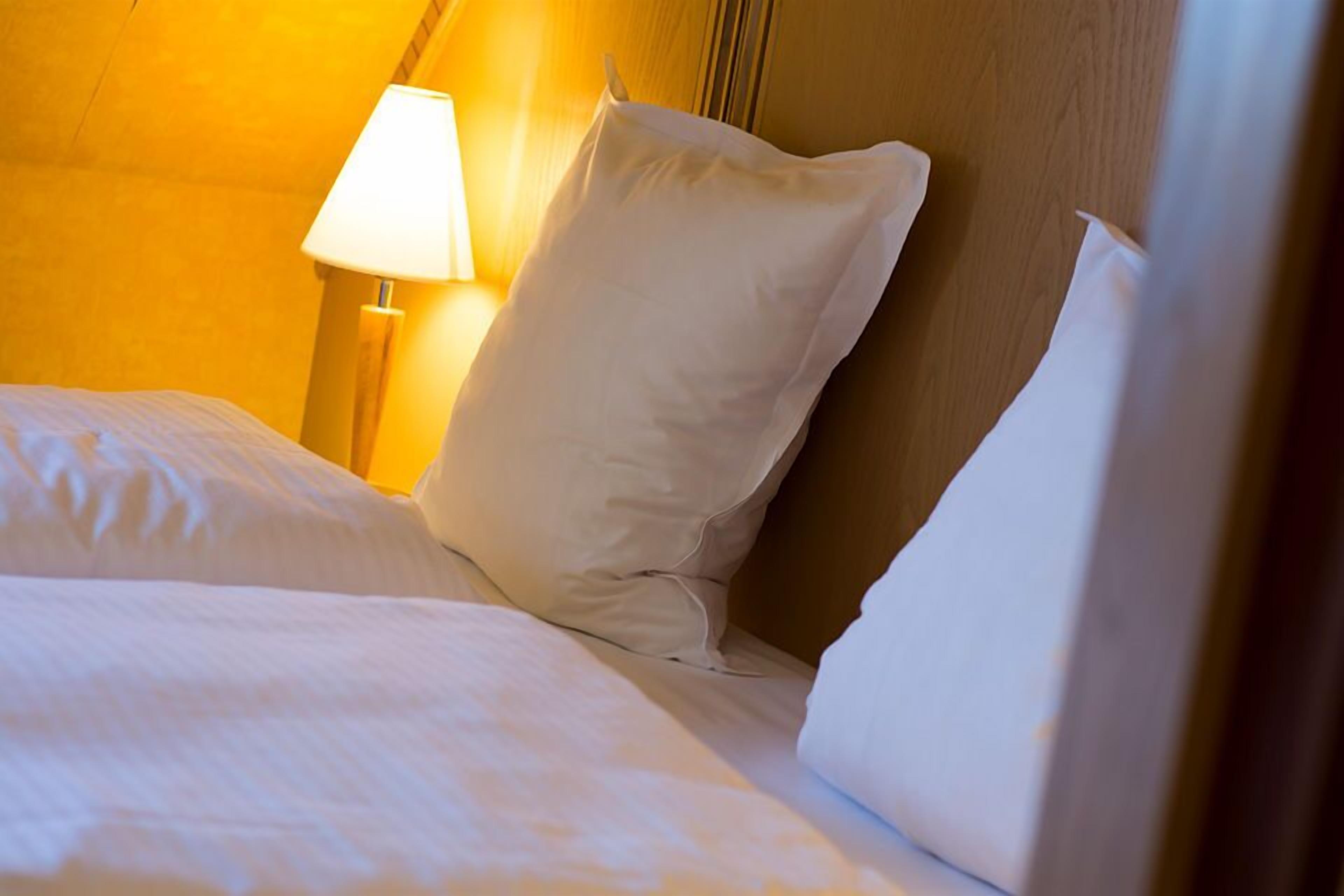 A neatly made bed with white linens and pillows, a bedside lamp, and a wooden headboard.